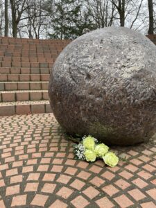 Bild vom Denkmal GEDENKEN. Eine deformierte Abrisskugel in einem runden Areal, das ähnlich einem griechischen Theater stufenweise aufgebaut ist. Vor der Kugel liegen helle Blumen