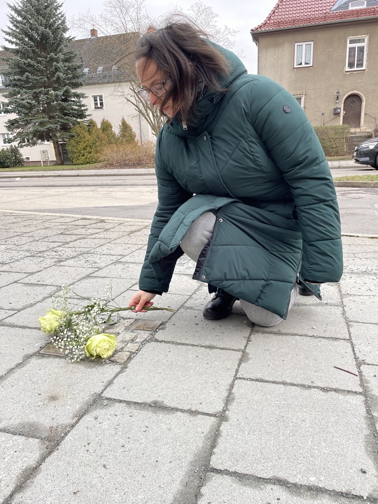 Frau kniet vor Stolperstein Gedenkstein und legt Blumen zum Gedenken nieder