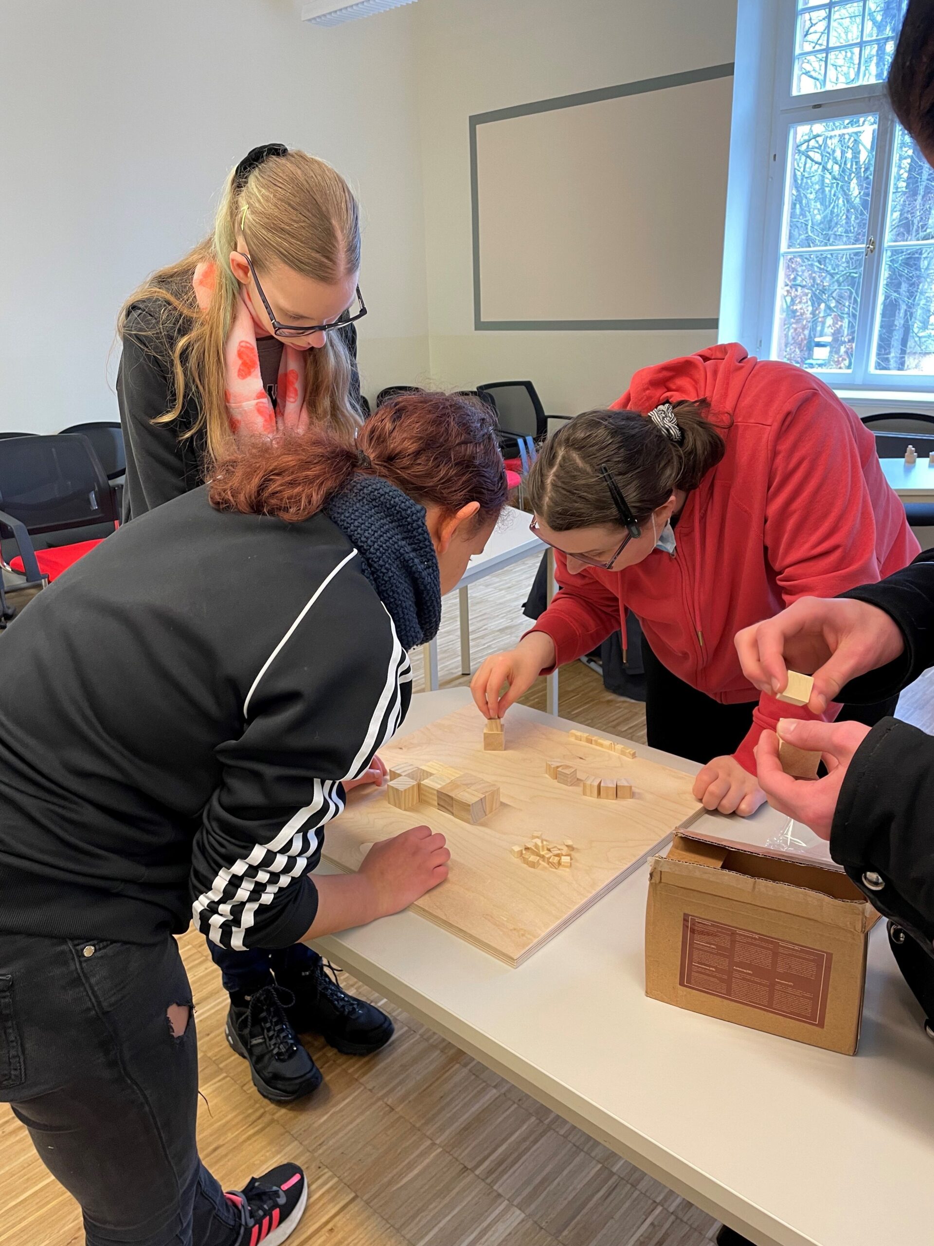 Eine Gruppe junger Menschen, die an einem Tisch an einem Holzrelief arbeiten 