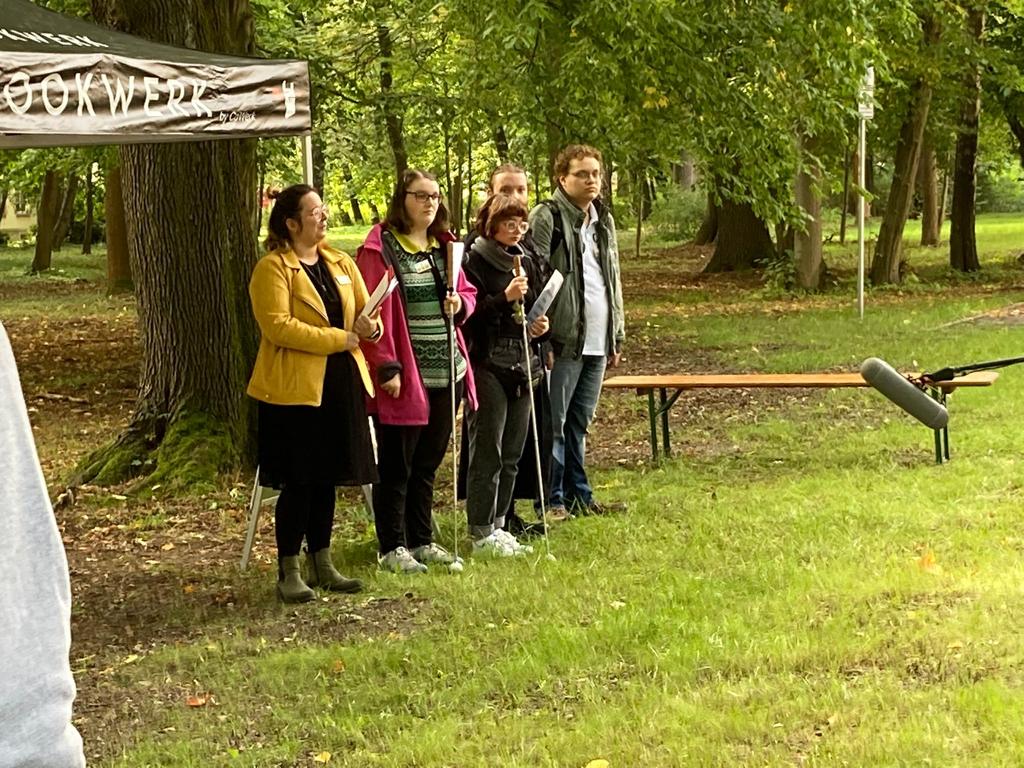 Auszubildene und Frau Schmidt begrüßen die Gäste, auf Wiese vor Baum