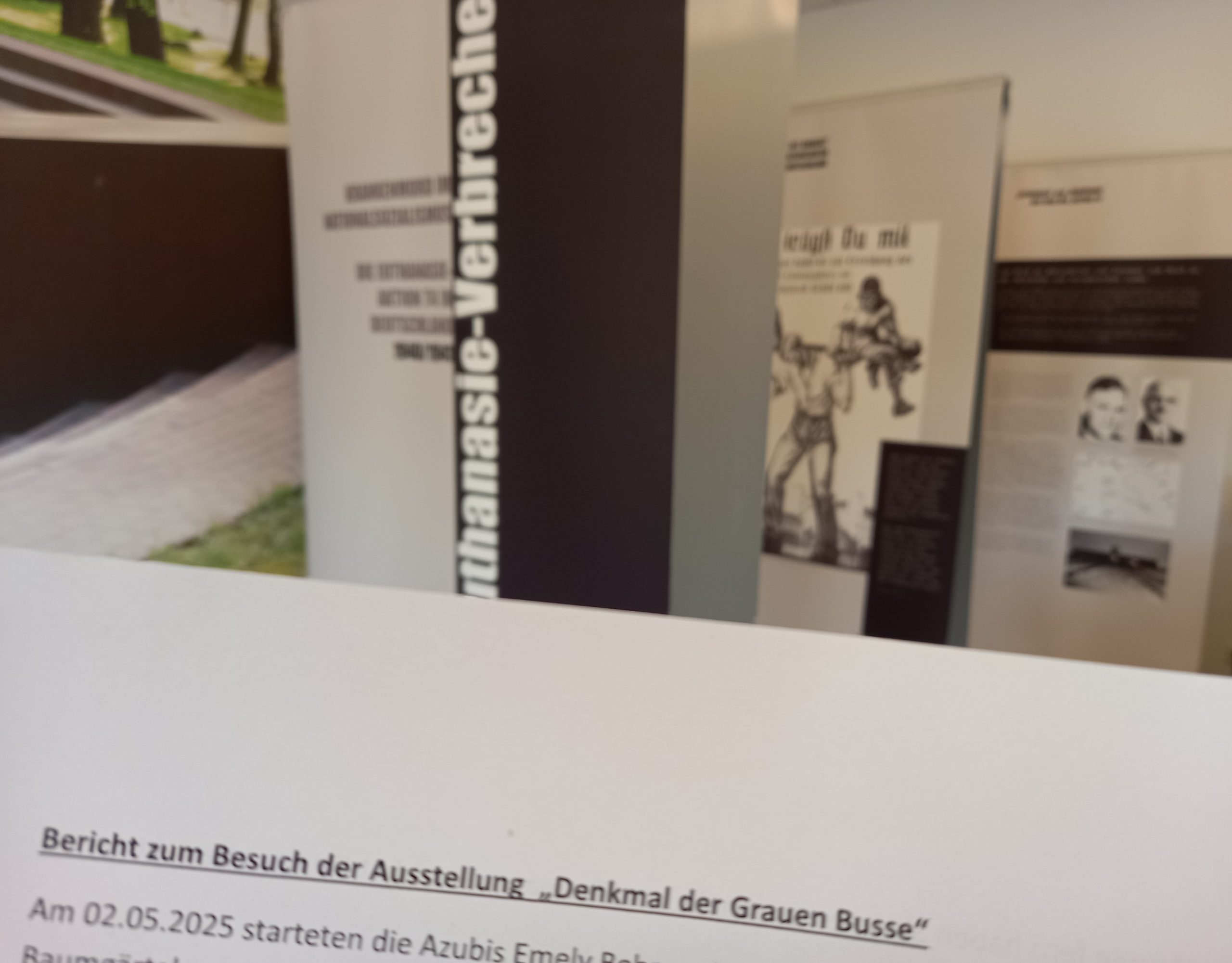 Im Vordergrund ist die Überschrift eines Berichts zu sehen. Dahinter kann man schemenhaft die Ausstellung erkennen.