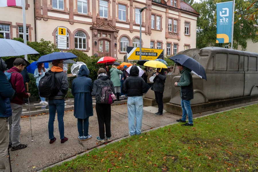 Schülerinnen und Schüler, Auszubildende und Mitarbeitende aus dem Rehabilitationszentrum haben sich für die Gedenkaktion rund um das Denkmal der Grauen Busse versammelt.