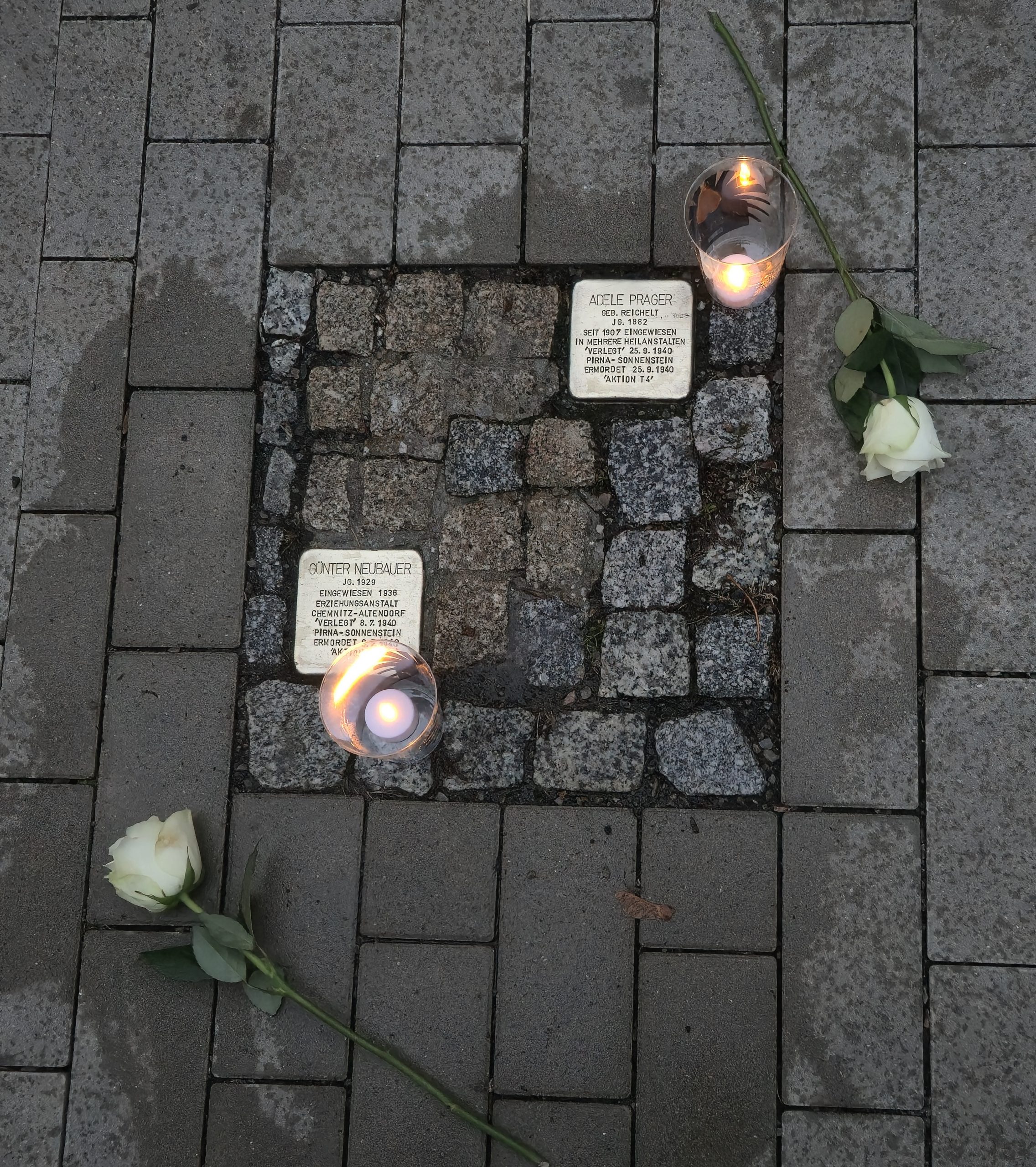 Die beiden Stolpersteine für Adele Prager und Günter Neubauer, gereinigt, beleuchtet und mit weißen Rosen geschmückt.